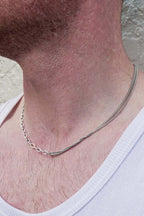 Silver chain necklace on a person wearing a white shirt against a neutral background