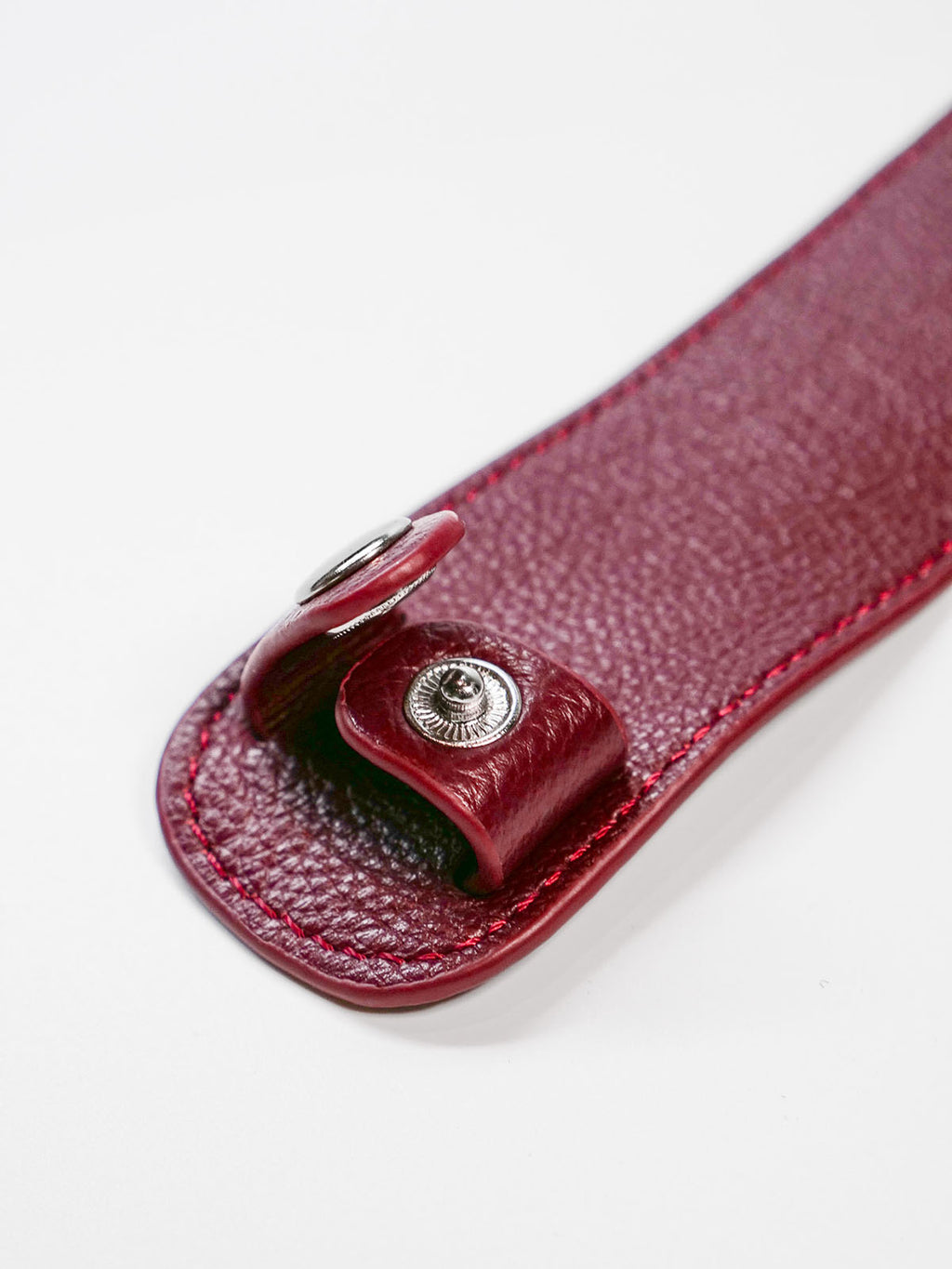 Close-up of a red leather strap with a metal button on a white background