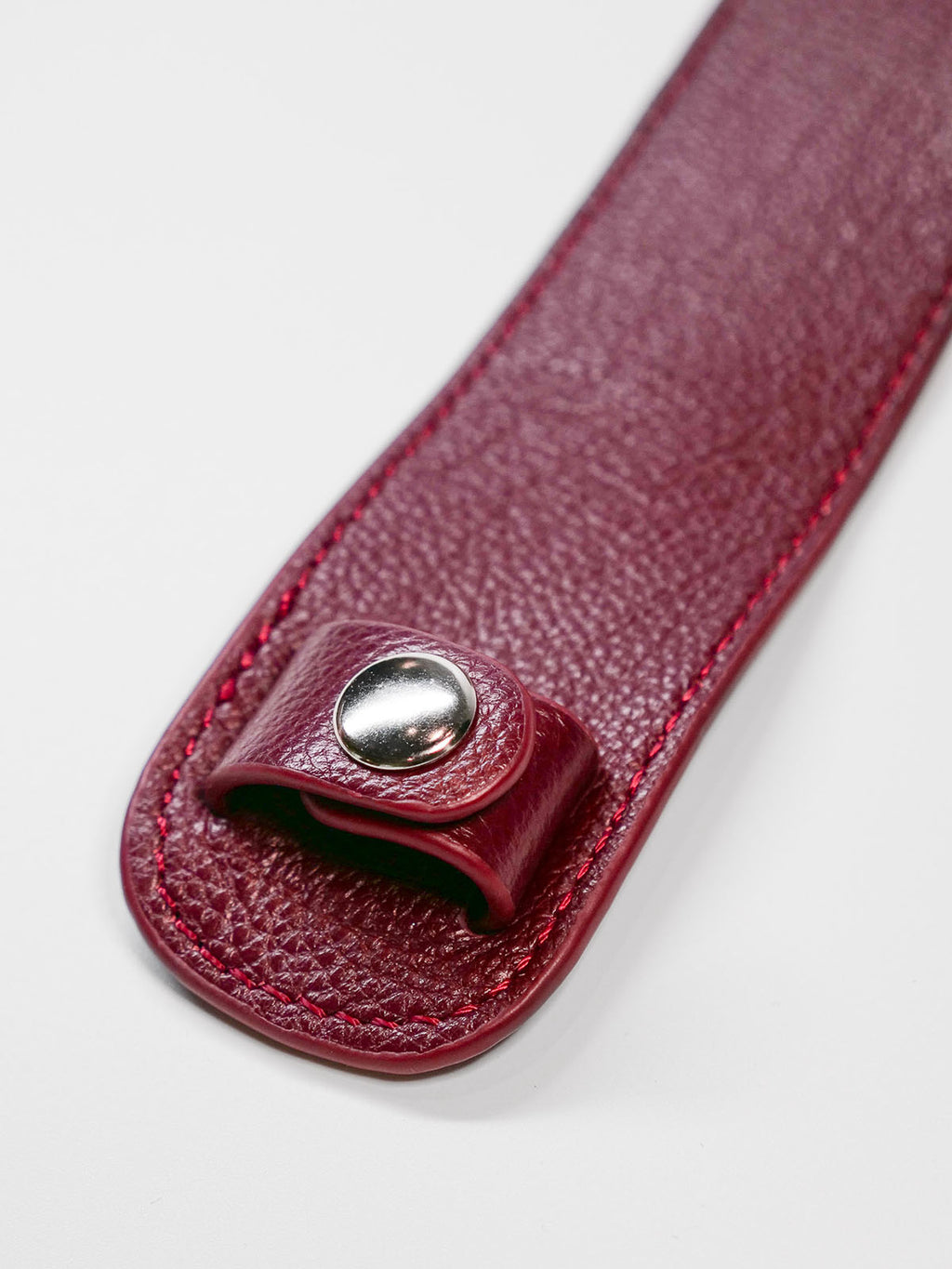 Close-up of a red leather strap with a silver button on a white background