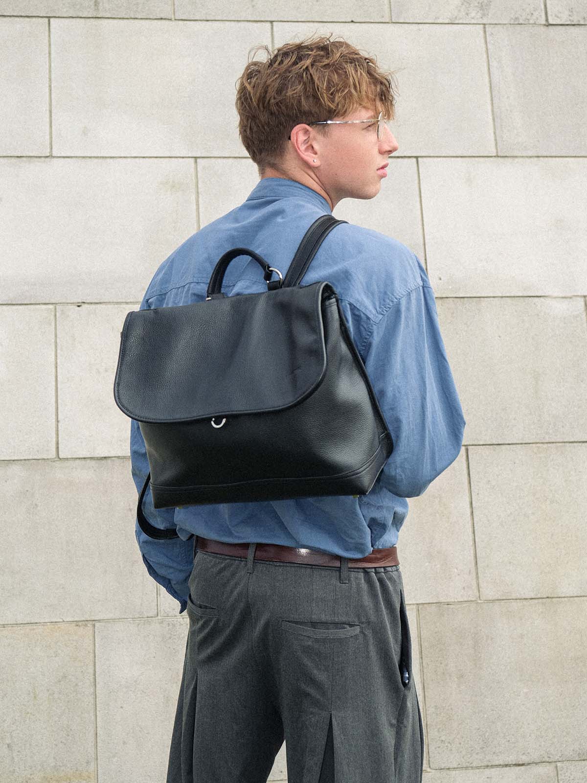 Black Amari top grain leather backpack worn on one shoulder on back