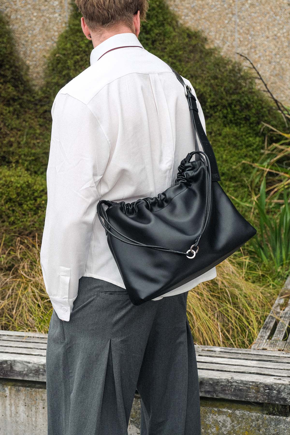 Man wearing a black drawstring bag over his shoulder outdoors.