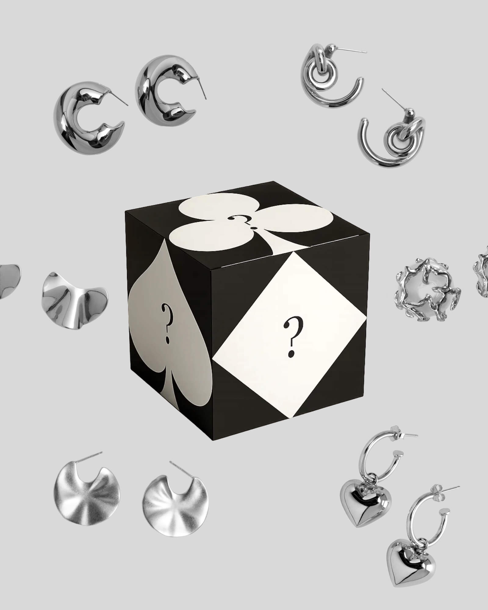 Black and white box with question marks surrounded by silver earrings on a light gray background