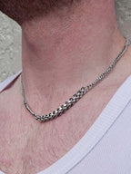 Close-up of a silver chain necklace on a person's neck with a neutral background