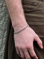Hand wearing a silver chain bracelet with a stone wall background