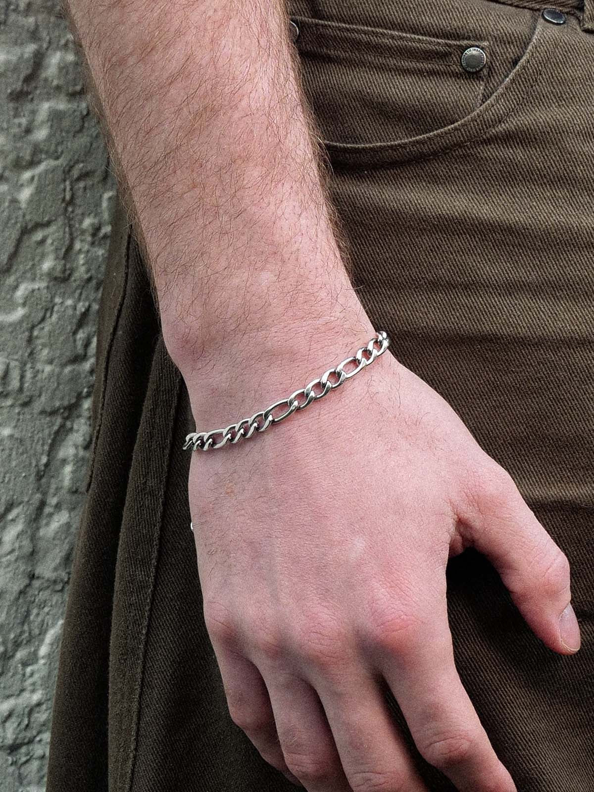 Hand wearing a silver chain bracelet with a stone wall background