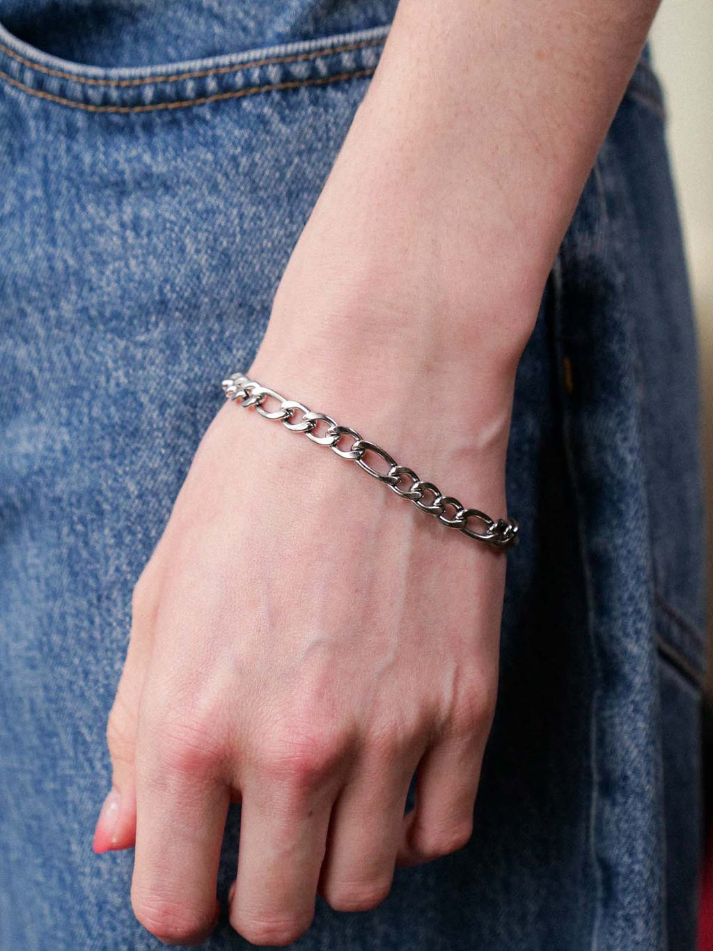 Silver chain bracelet on a wrist with a denim background
