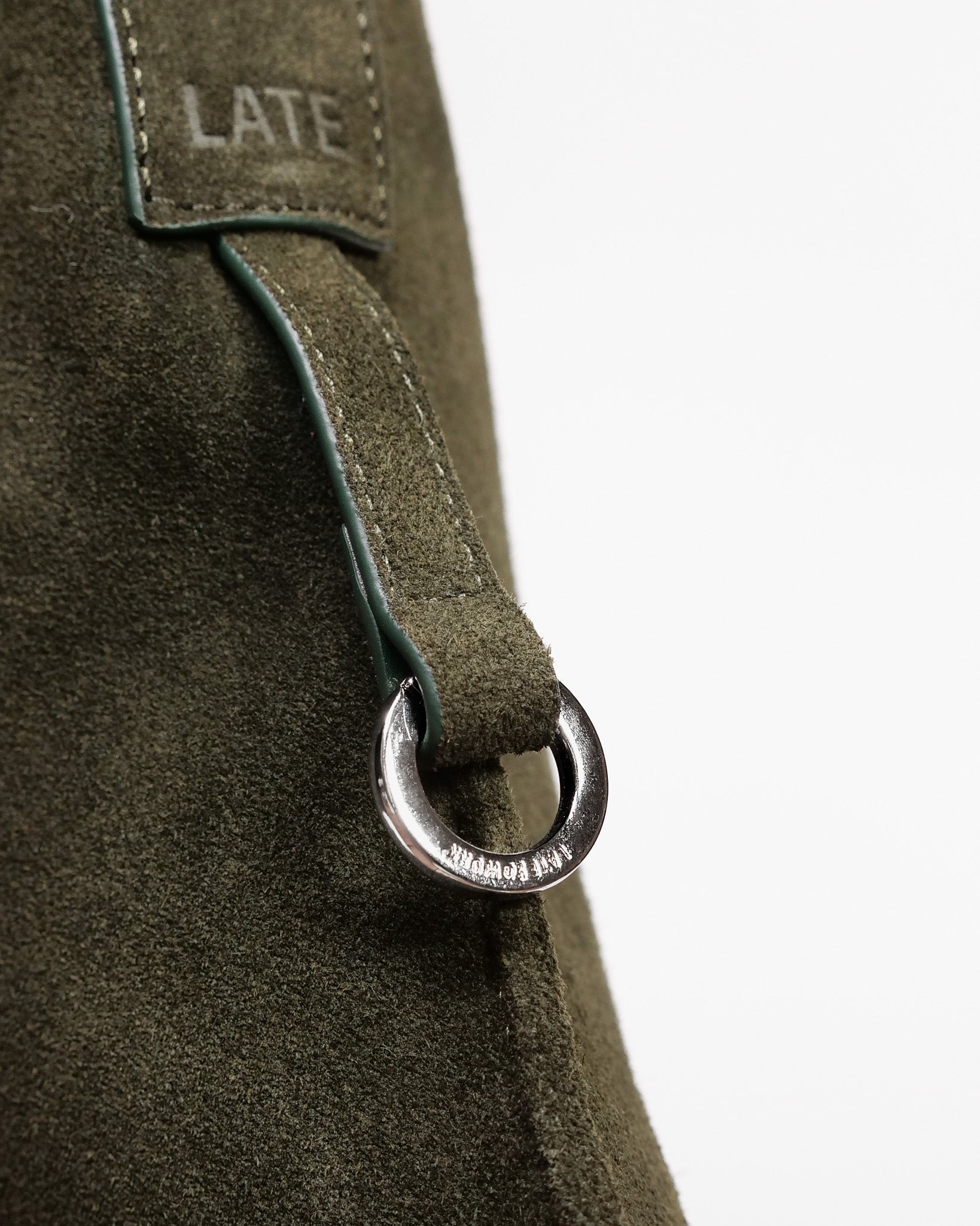 Close up of silver 'Late to Work' embossed ring on the forest suede medium Kite Bag