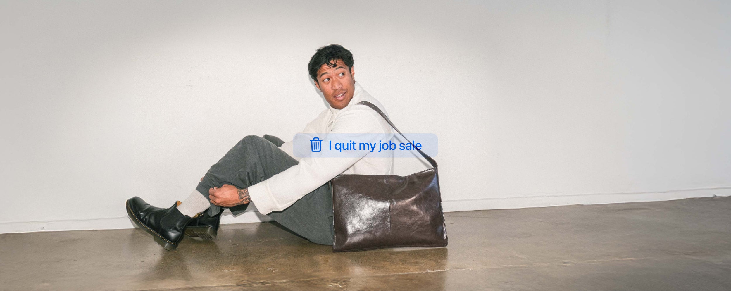 Person sitting on the floor wearing the Brown Kite Bag on shoulder. 