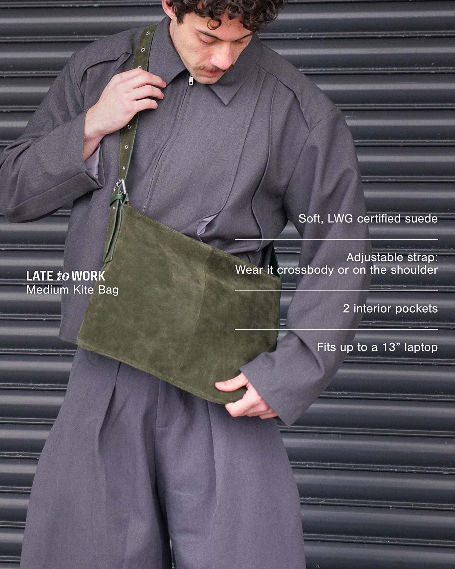 A man wearing a dark gray oversized jacket and pants carries a muted olive green suede crossbody bag.The image features text overlays detailing the bag's features (medium kite bag, soft LWG certified suede, adjustable strap, 2 interior pockets, fits up to a 13" laptop).
