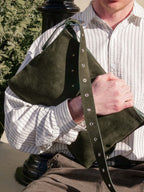 Man holding medium forest suede Kite Bag under one arm with the strap hanging down.