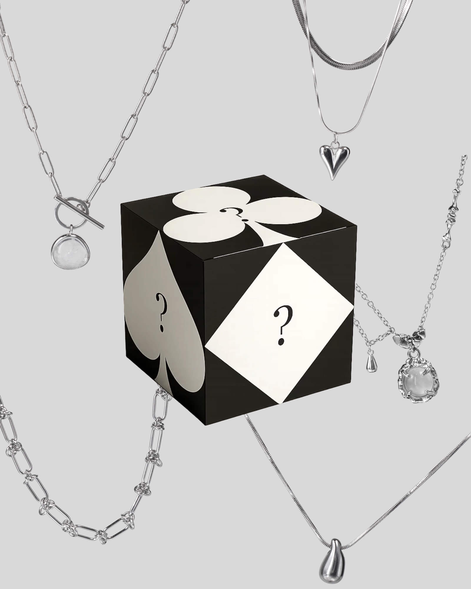 Black and white box with question marks surrounded by silver necklaces on a light gray background