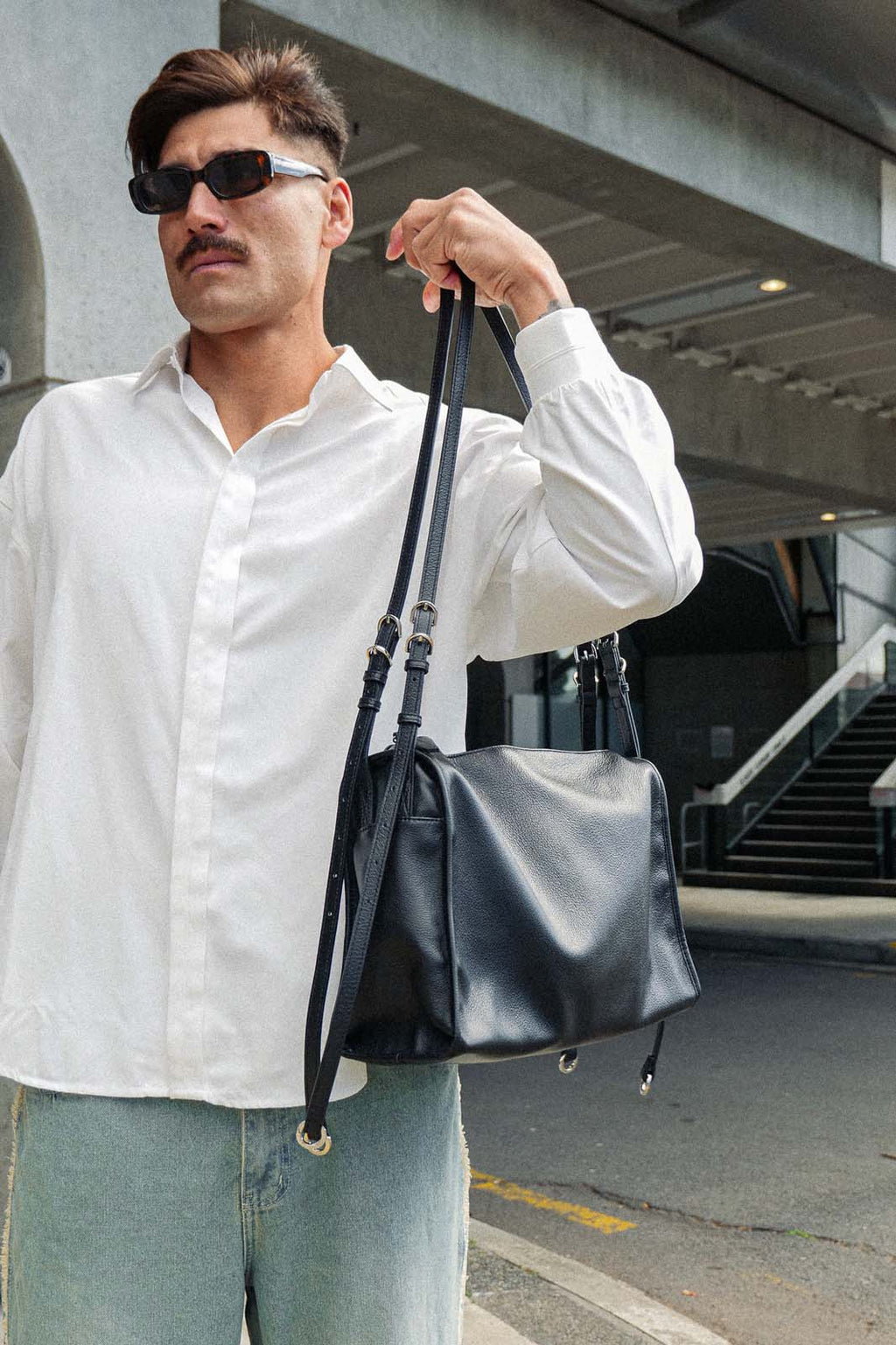 Man holding a black leather bag outdoors