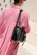 Person wearing a pink outfit with a black leather bag on a light-colored wall background