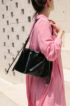 Person wearing a pink outfit with a black handbag against a light-colored wall.