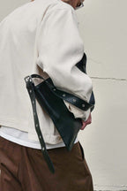 Person holding black medium Kite Bag under one arm against a plain wall