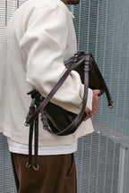 Person holding a brown leather bag against a metal fence background