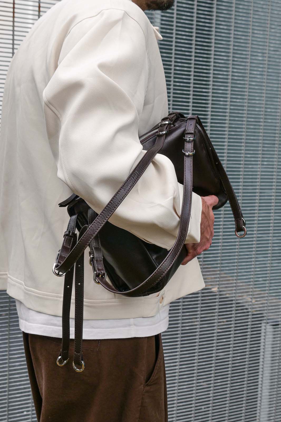 Person holding a brown leather bag against a metal fence background