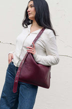 Woman holding a burgundy leather bag against a light gray wall