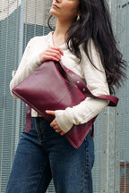 Woman holding a burgundy leather bag against a metallic background