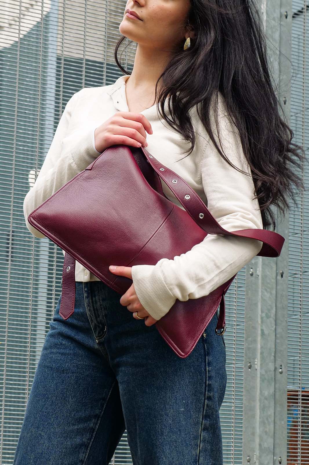 Woman holding a burgundy leather bag against a metallic background