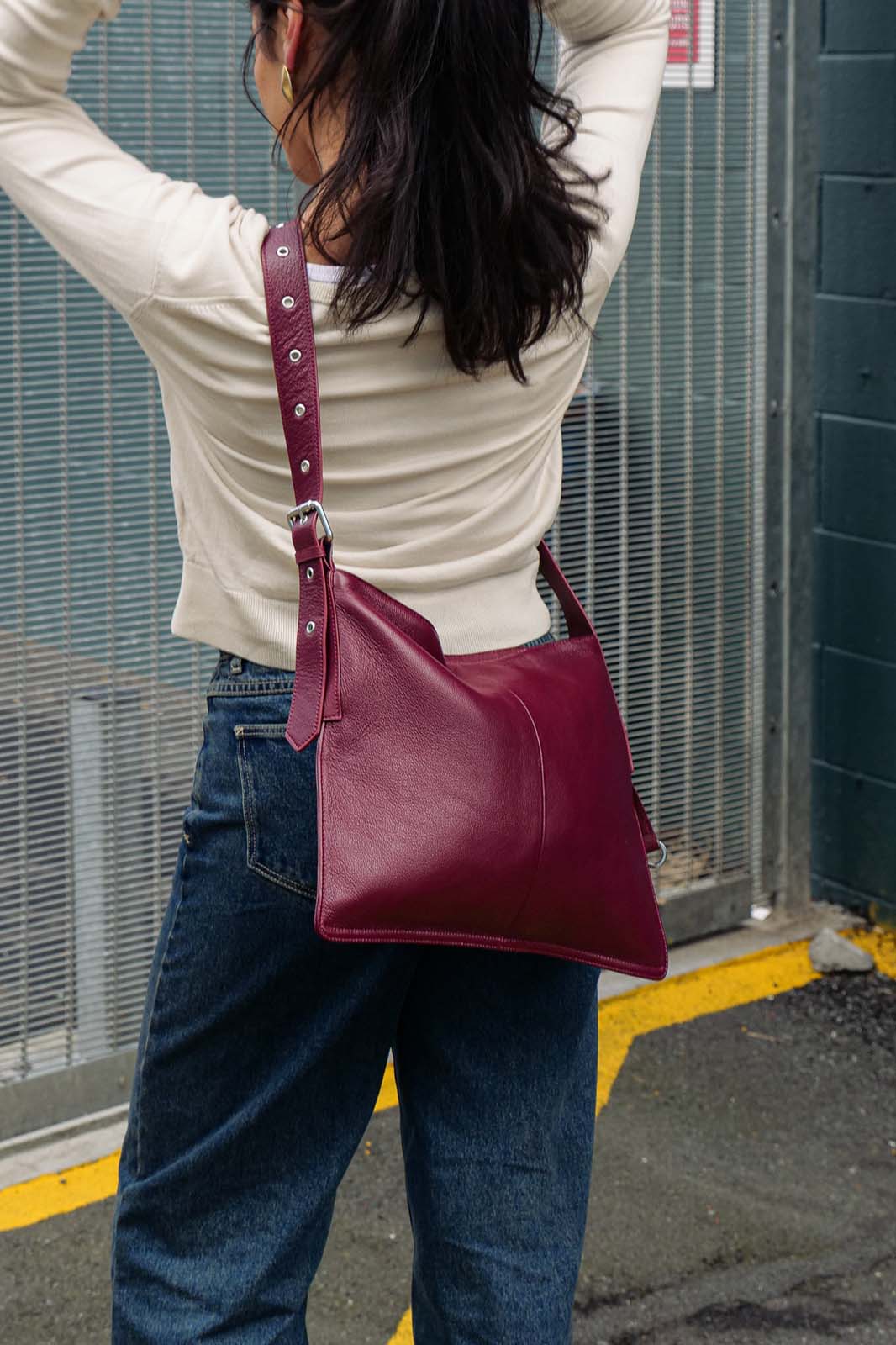 Person wearing a burgundy bag crossbody in an urban setting