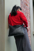 Person wearing the black medium Luxe Kite Bag crossbody against a brick wall