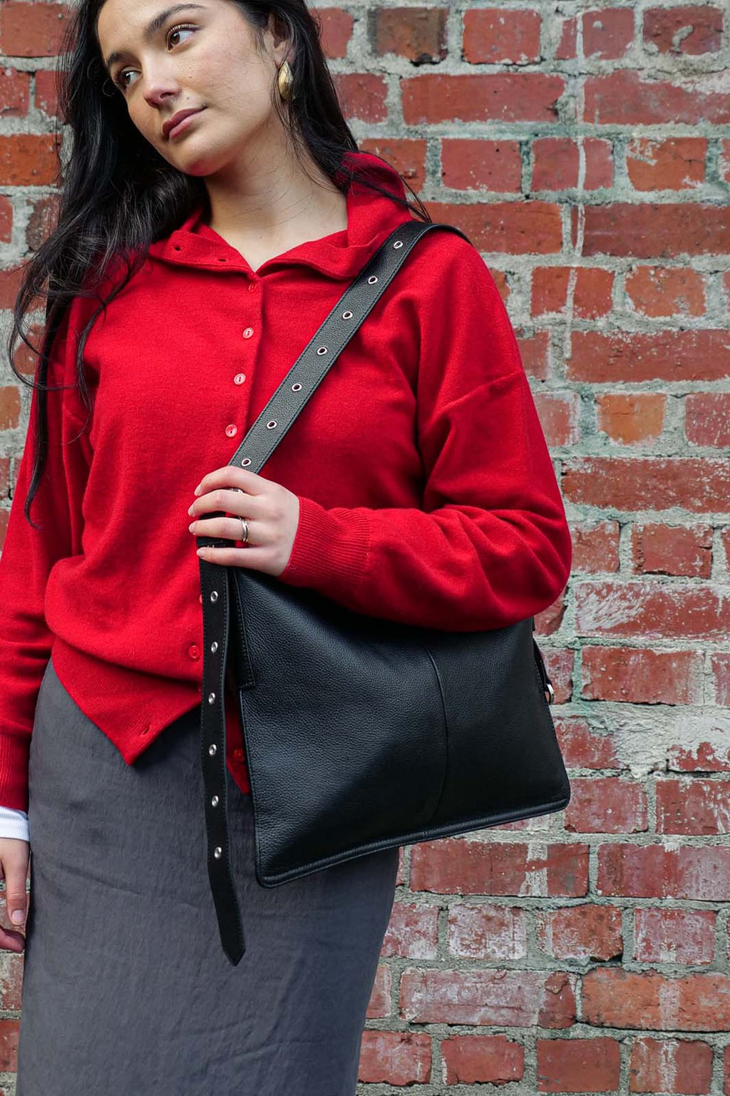Woman in red sweater wearing medium Luxe kite Bag on one shoulder against a brick wall