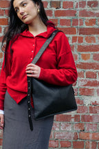 Woman in red sweater wearing medium Luxe kite Bag on one shoulder against a brick wall