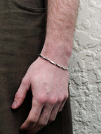 Hand wearing a silver bracelet against a neutral background