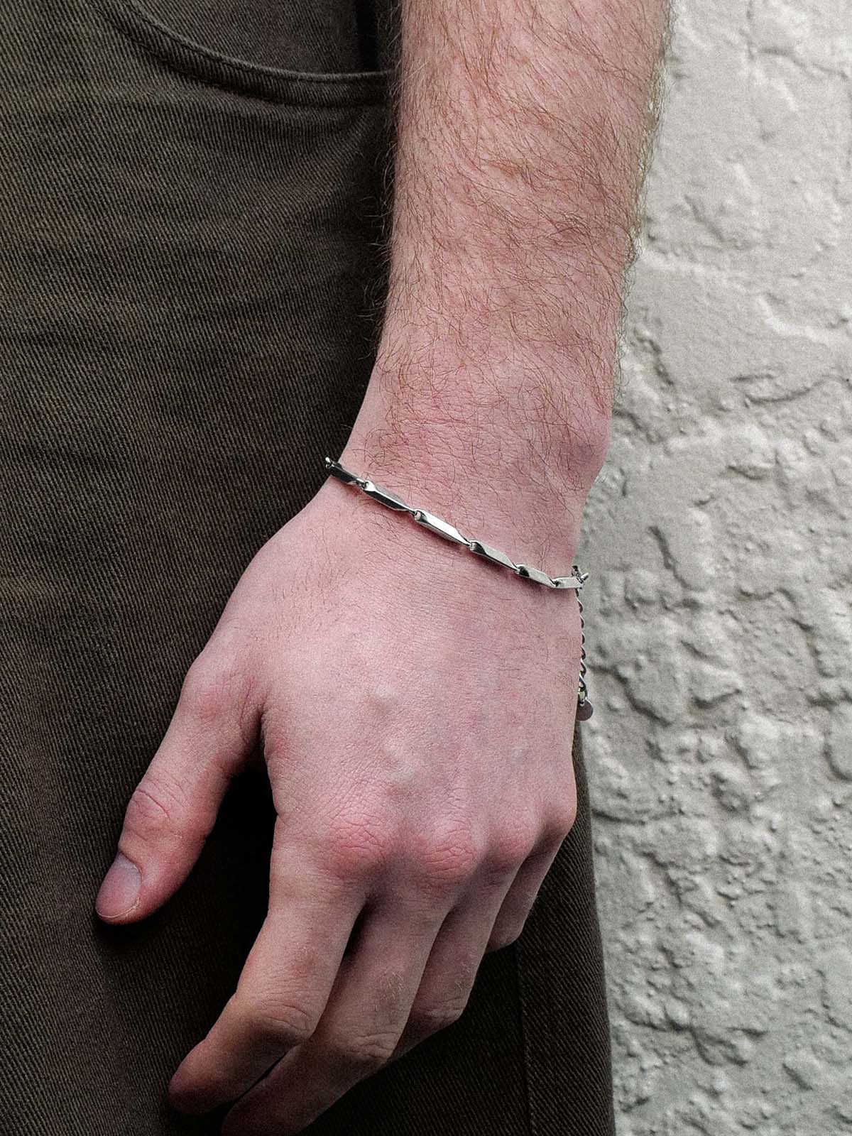 Hand wearing a silver bracelet against a neutral background