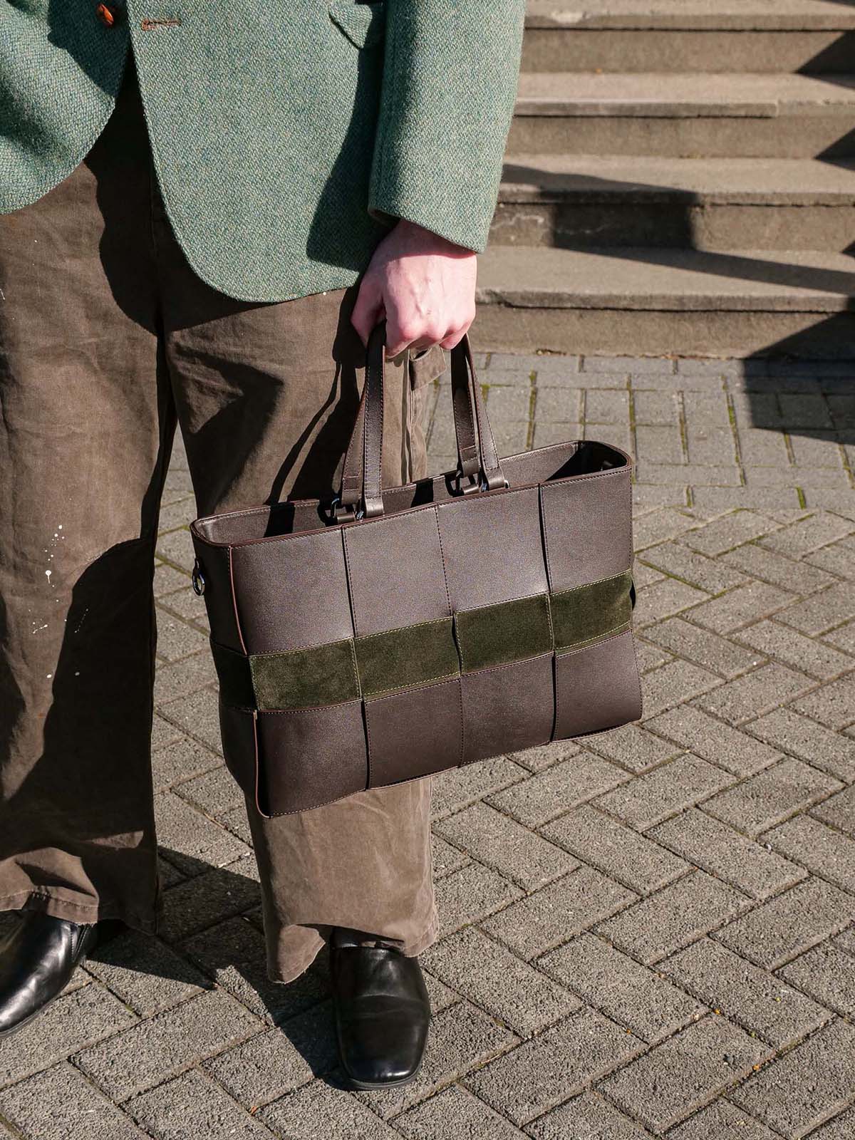 Reed Woven Bag in Forest and Walnut held by a mans leg by its top handles