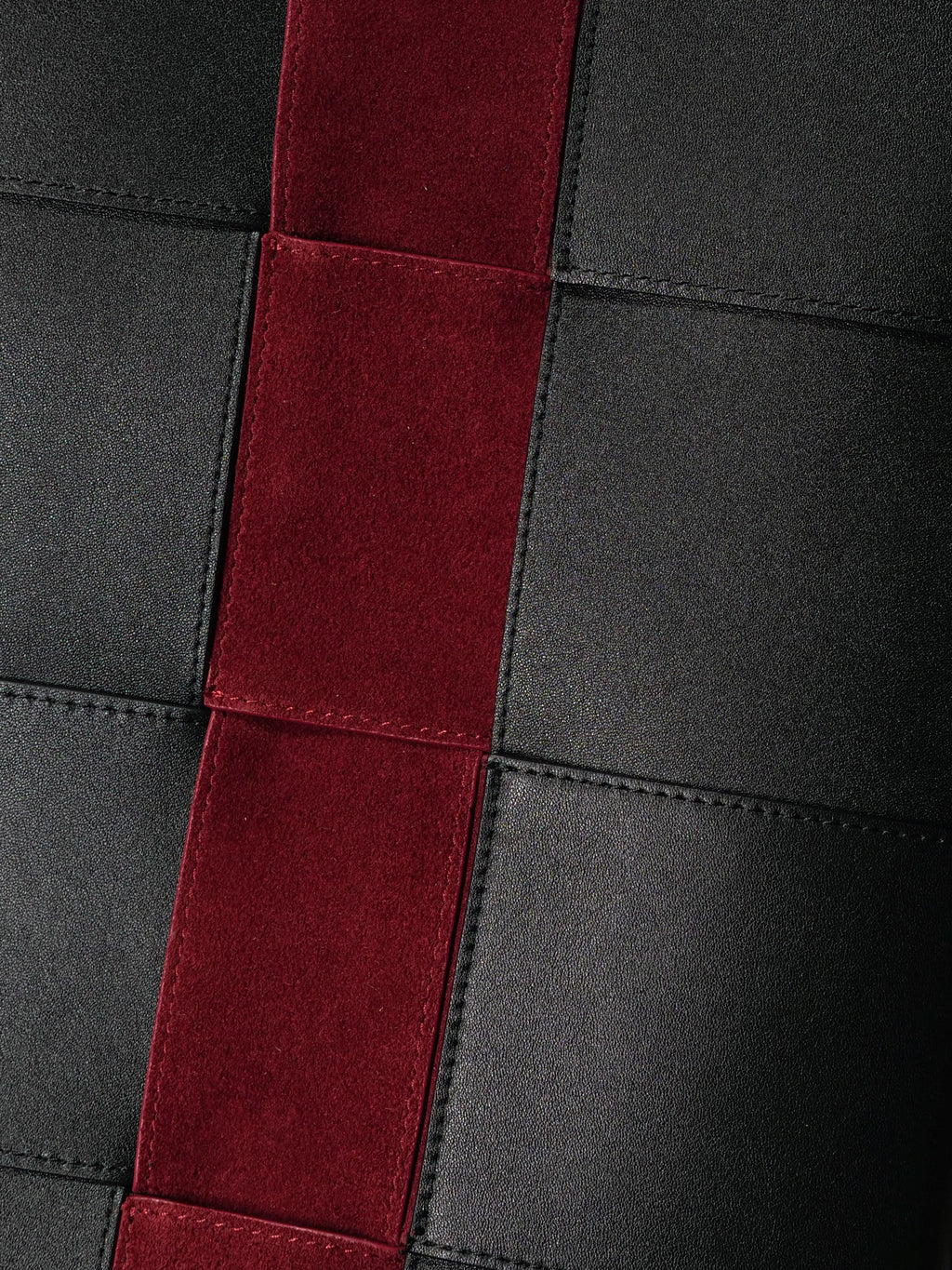Close-up of a leather bag featuring black panels and a prominent vertical red suede stripe.