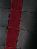 Close-up of a leather bag featuring black panels and a prominent vertical red suede stripe.