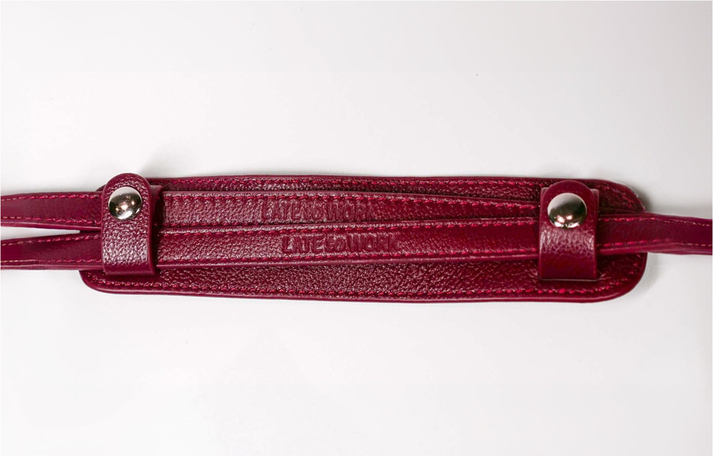 A close-up of a burgundy textured leather strap with metal snap buttons on a white background.