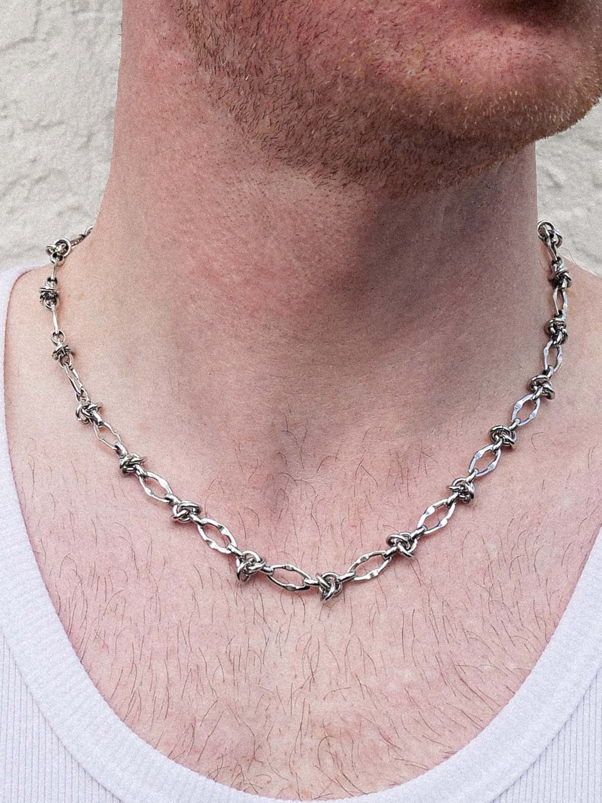 Silver chain necklace worn by a person with a neutral background