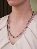 Silver chain necklace worn by a person against a neutral background