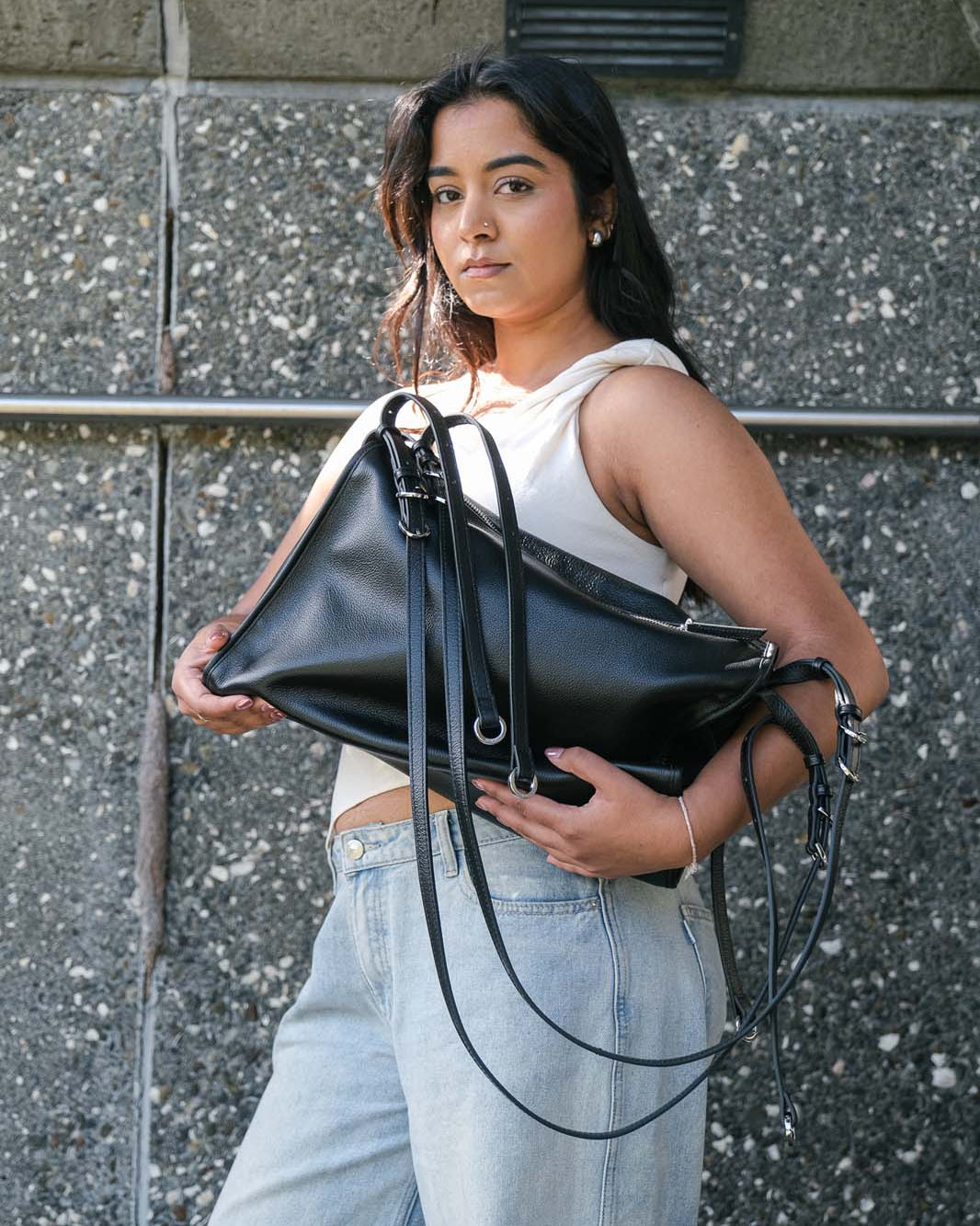 Woman holding a black leather handbag against a gray wall.