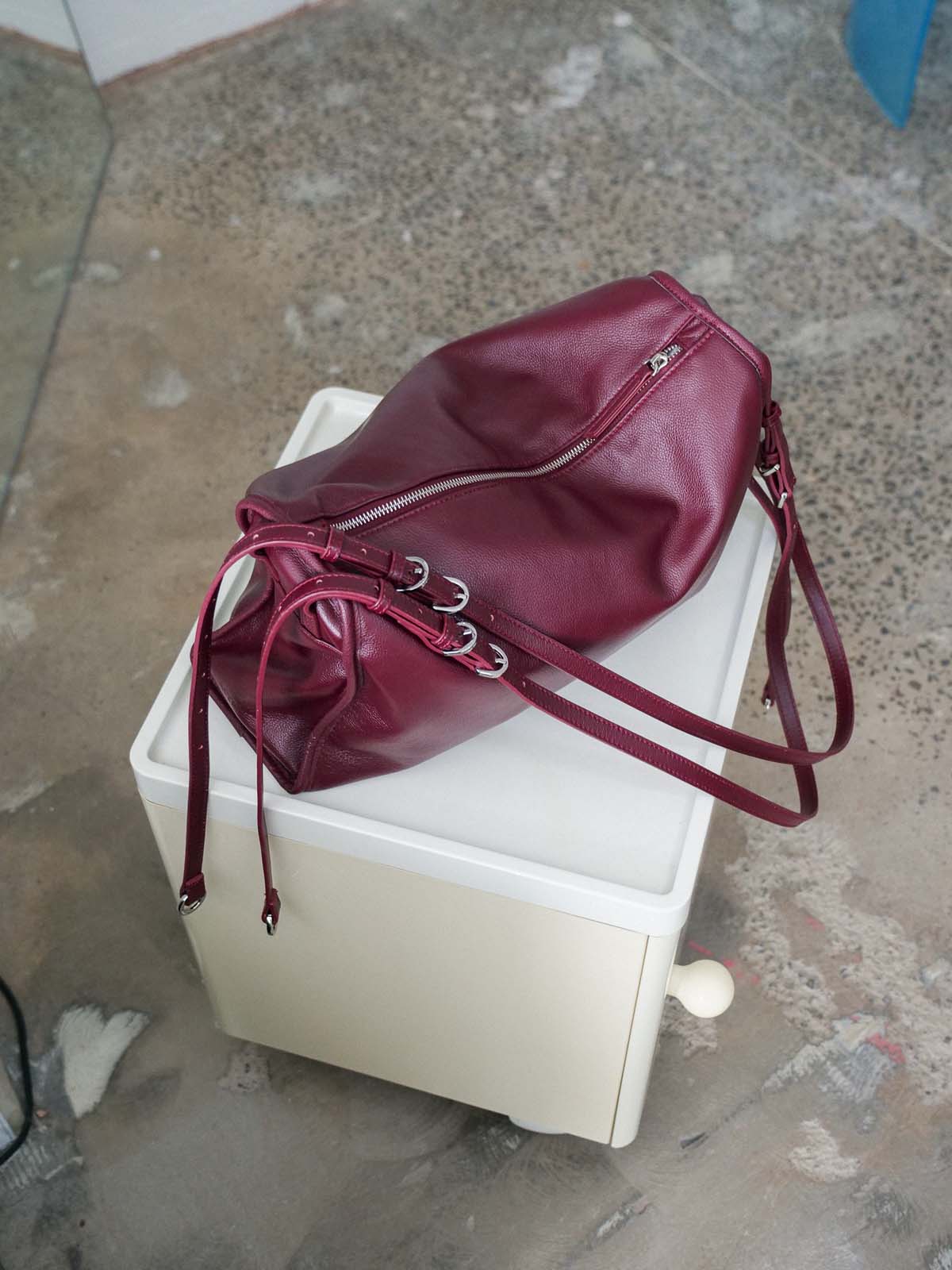 Burgundy Willow bag with silver hardware resting on top of a white plastic storage box on a concrete floor.