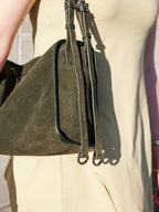 Close-up of a person wearing a cream-colored dress and carrying an olive green suede shoulder bag with dark trim and long straps.