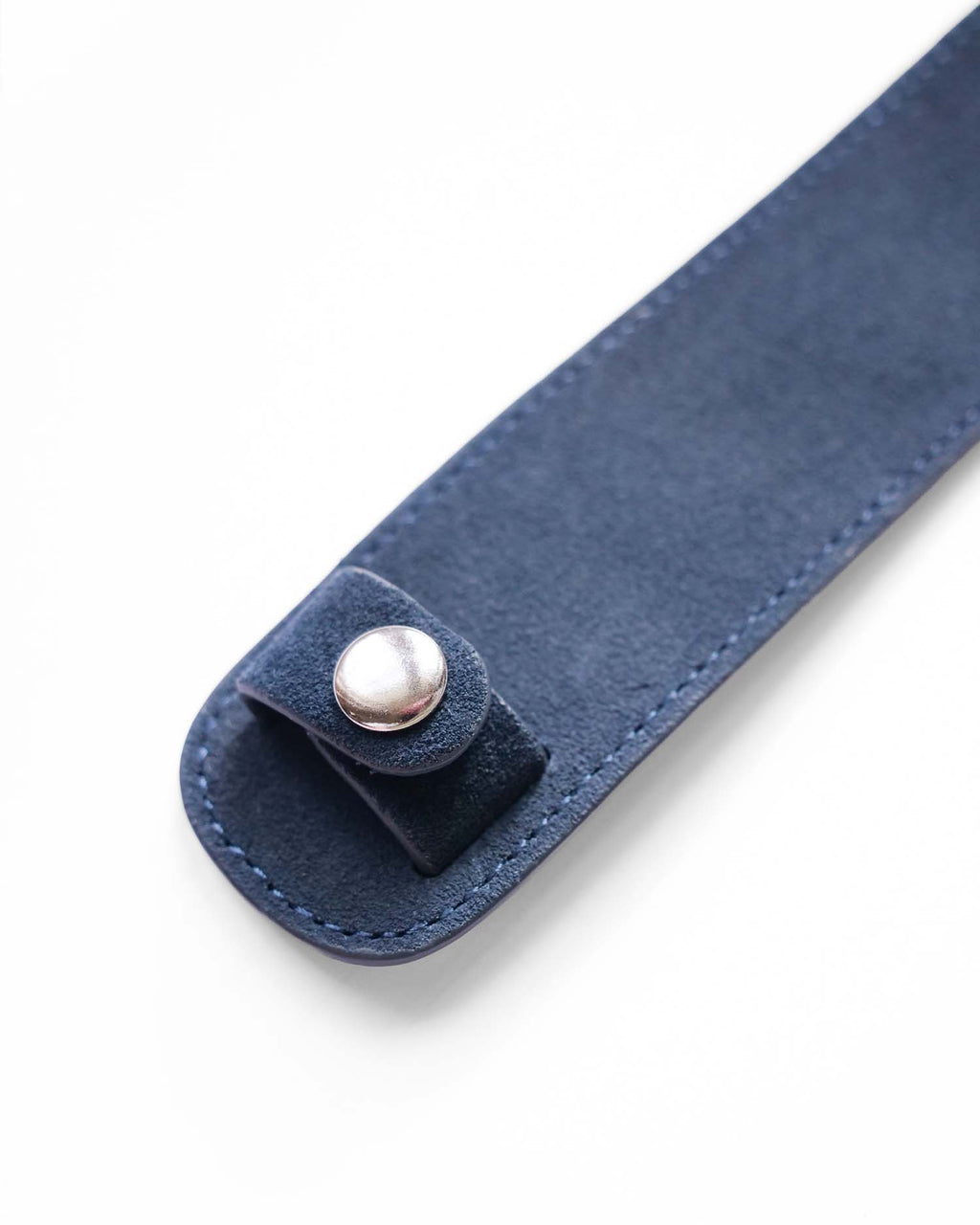 A close-up of a navy blue shoulder pad,, featuring a matching leather tab with a silver metal snap button closure, set against a plain white background.